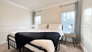 Ein Schlafzimmer mit Bett, Nachttisch, Vorhängen am Fenster und Blick auf Bäume.