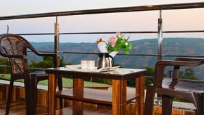 A balcony with a wooden table, two chairs, a vase with flowers, and a metal pitcher. - Melody 24 East Resort (Mahabaleshwar)