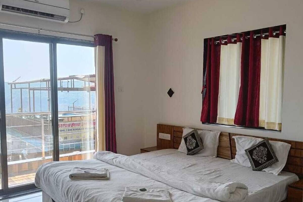 A hotel room with a large bed, a ceiling fan, a window with curtains, and a view of a pool and building.