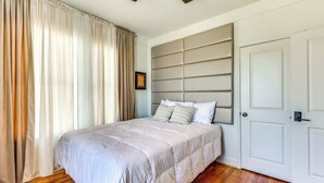 A bedroom with a large bed, a headboard, a door, and wooden flooring.
