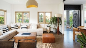 A modern living room with a sofa, coffee table, and ottoman, a large plant, and a dining area with a table and chairs. - Bellevue Berawa Managed by CPM Bali (Canggu)
