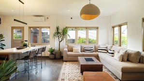 A spacious living area with a sofa, ottoman, and coffee table, a dining area with chairs and a table, and large windows providing natural light. - Bellevue Berawa Managed by CPM Bali (Canggu)