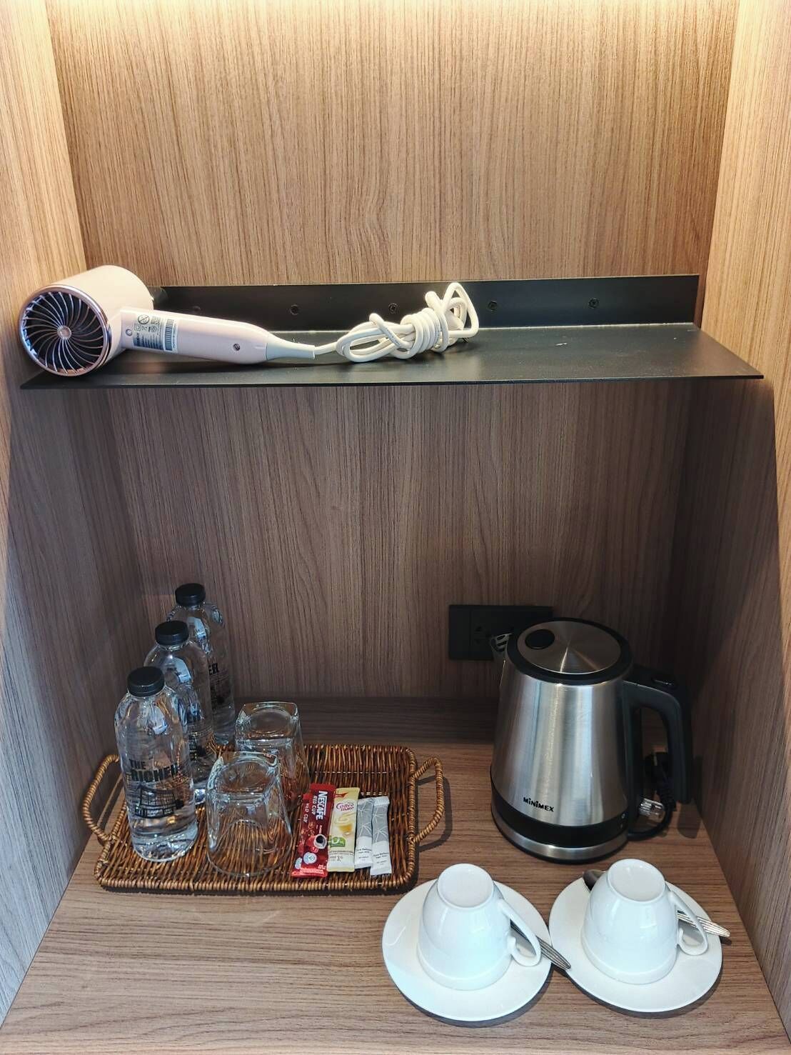 Una habitación compacta con secador de pelo, tetera y bandeja con botellas de agua y vasos.