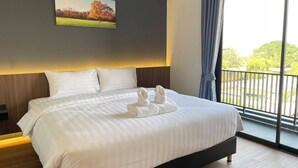 Une chambre d’hôtel avec un grand lit, un tableau au mur et une vue sur la verdure par la fenêtre.