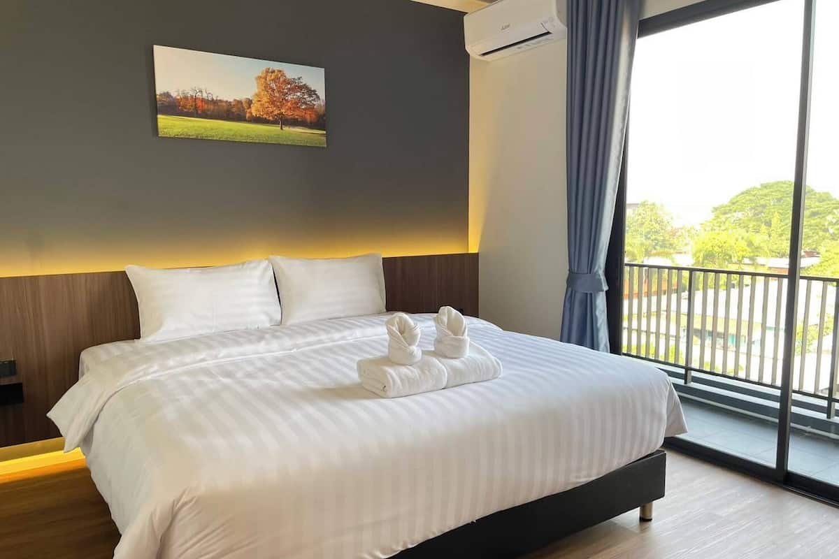 A hotel room with a large bed, a painting on the wall, and a view of greenery through the window.