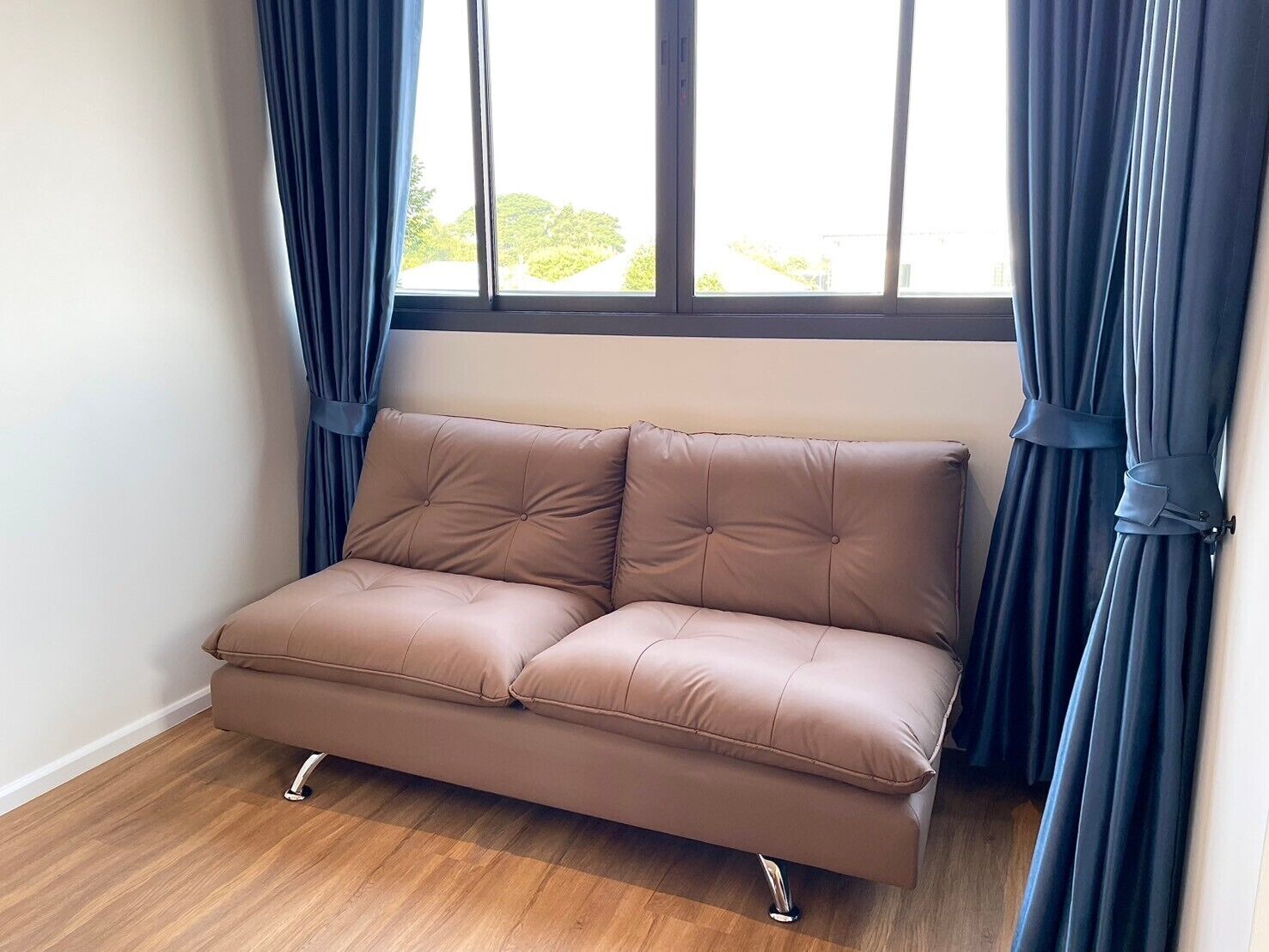A brown leather sofa with a tufted backrest and armrests, positioned against a window with dark curtains.
