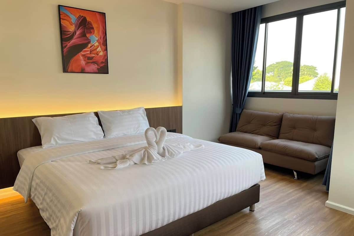 A hotel room with a large bed, a sofa, a painting on the wall, and a window with curtains.