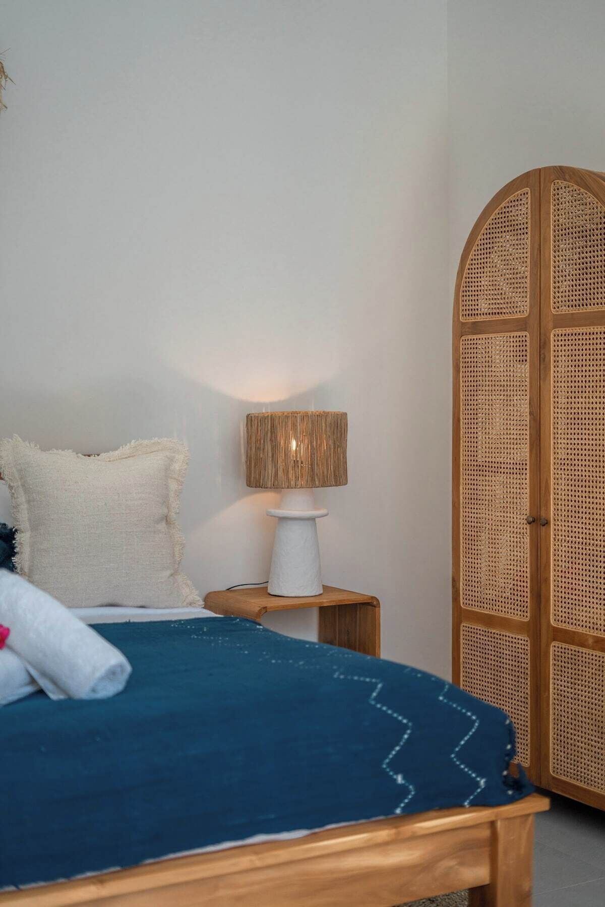 A bedroom with a bed, a bedside lamp, a wardrobe, and a wall-mounted shelf.
