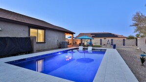 A swimming pool with a tiled deck, a covered patio area, and a building with a tiled roof in the background.