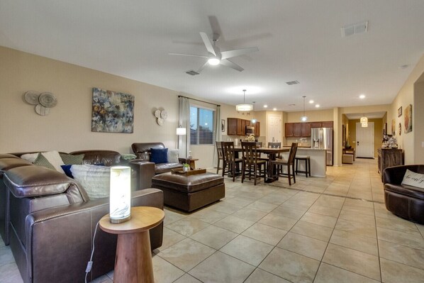 A spacious living room with leather sofas, a dining area with wooden chairs, and a kitchen in the background. - Desert Lynx 2, Beautiful Home, New Pool, Spacious Back Yard, 4 Bedroom 2 Bath! (Goodyear)