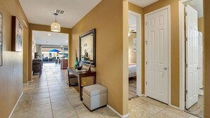 A hallway with a tiled floor, a desk with a vase, a mirror, and a door leading to a bedroom.