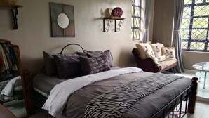 Quarto com cama, mesa de cabeceira e janela com cortinas.