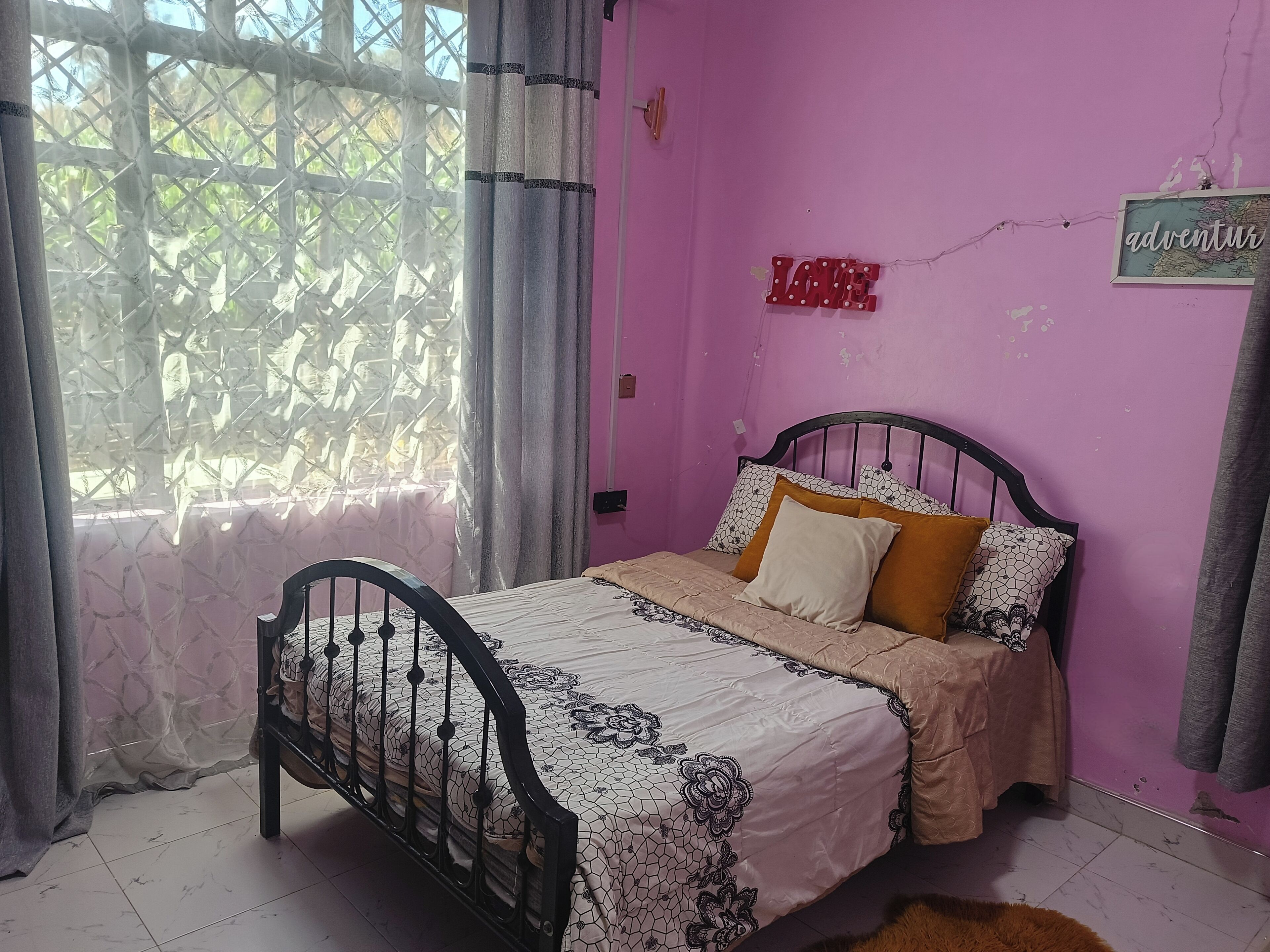 A bedroom with a bed, curtains, a window, and a wall with a sign.