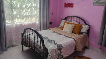 A bedroom with a bed, curtains, a window, and a wall with a sign.