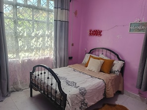 A bedroom with a bed, curtains, a window, and a wall with a sign.