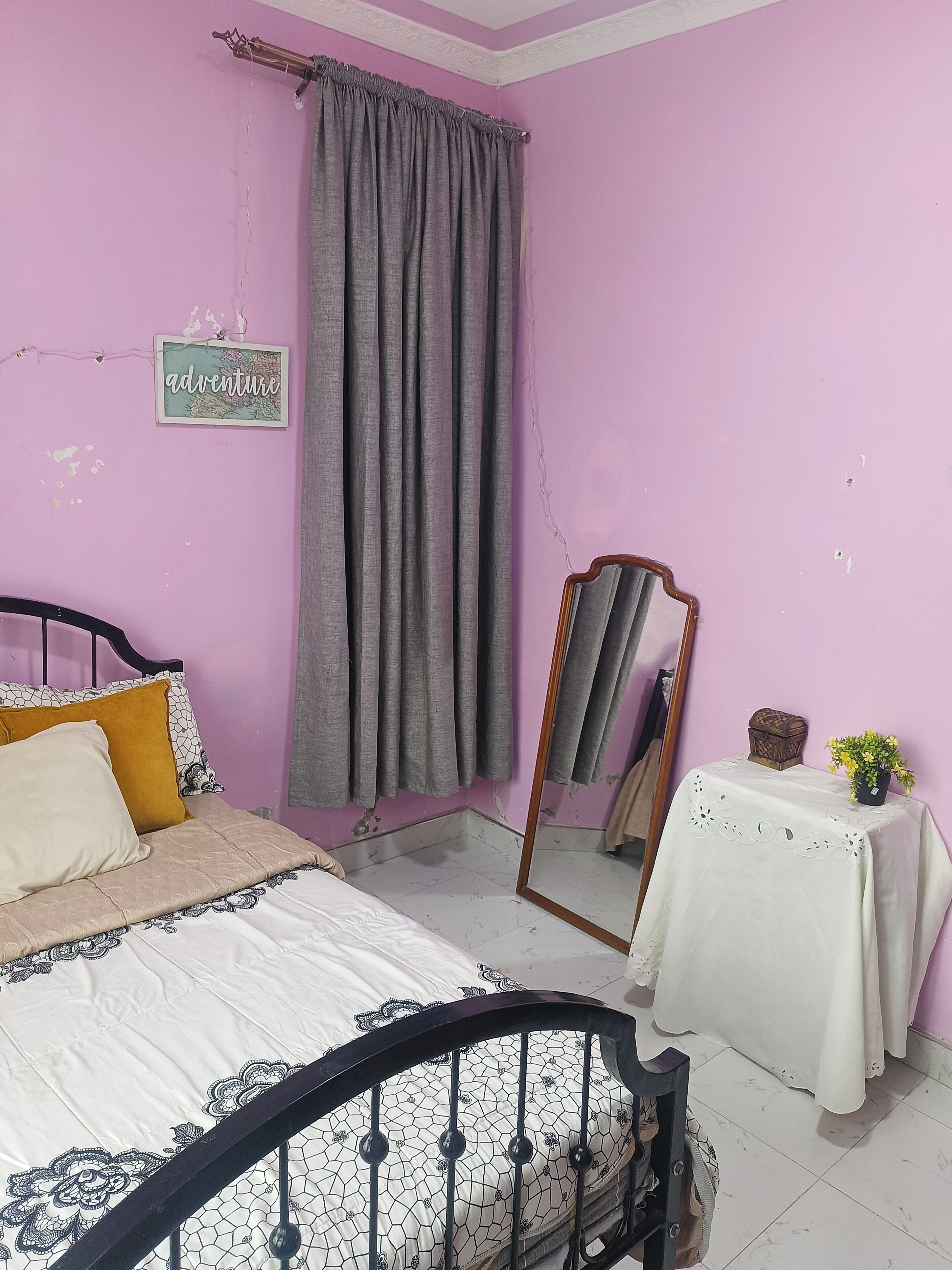 Una camera da letto con un letto, uno specchio, un tavolino con una pianta e un muro con un cartello.