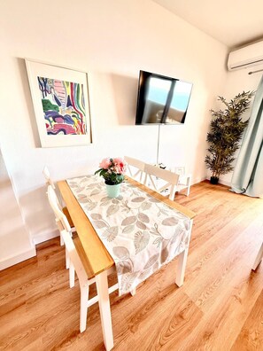 Ein Essbereich mit Holztisch und -stühlen, einem Blumentopf und einem an der Wand montierten Flachbildfernseher.