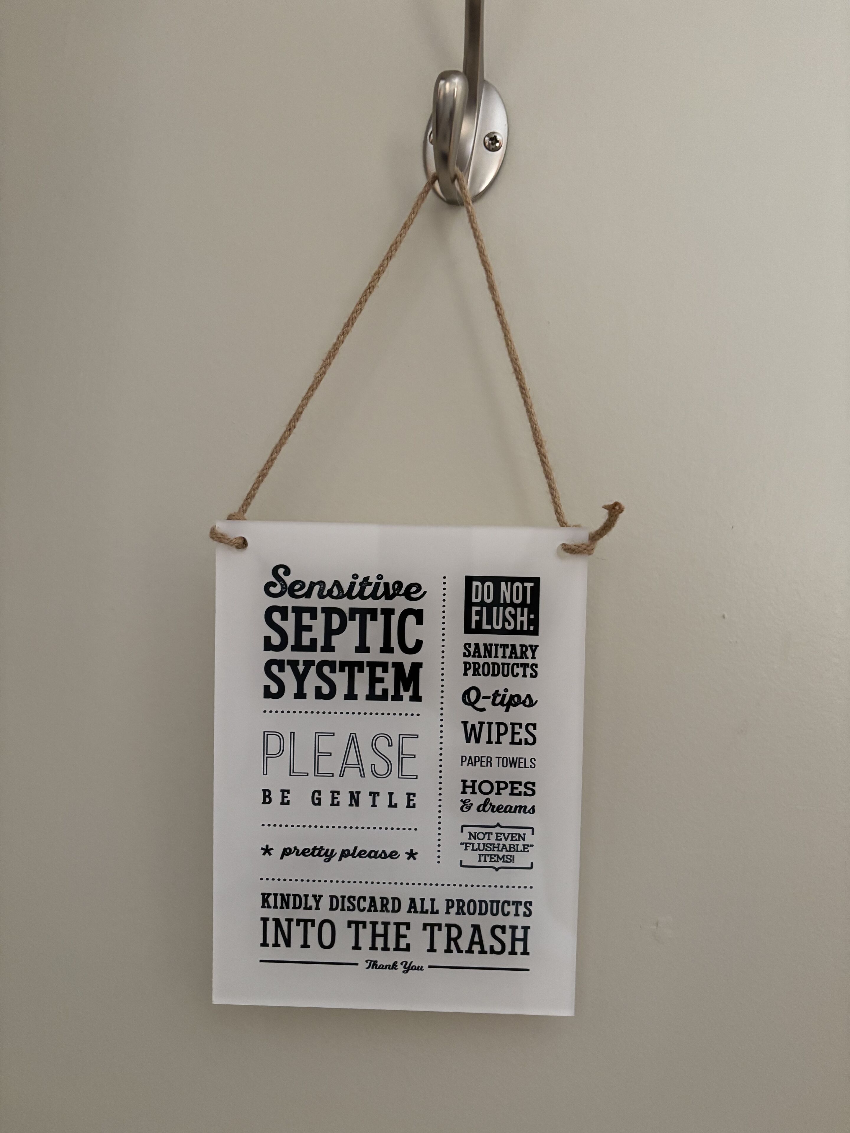 A sign hanging from a ceiling, advising against flushing certain items down the toilet.