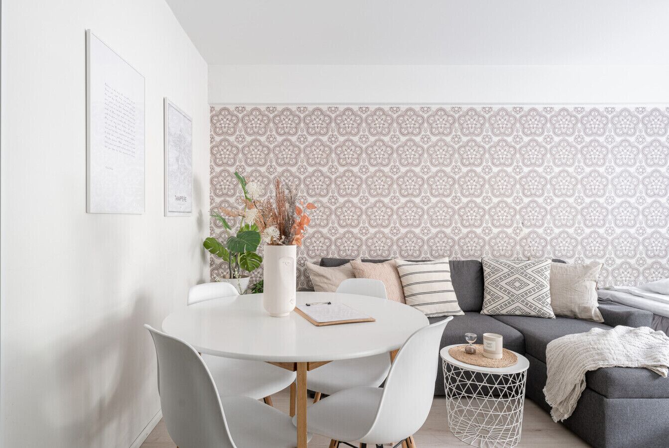 Una sala de estar moderna con una mesa de comedor redonda, sillas blancas, un sofá gris y papel tapiz estampado.