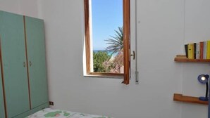A bedroom with a bed, a window with a view of the sea, a wardrobe, and a shelf with books. - ON THE WATERFRONT UNIQUE LOCATION!!!! (San Vito Lo Capo)