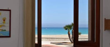 A room with a large window offering a view of a beach and the sea.