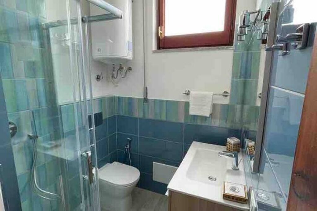 Casa de banho com cabine de chuveiro em vidro, sanita e lavatório com espelho.