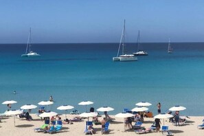 Une plage où l’on peut voir plusieurs voiliers sur l’eau et de nombreux parasols qui offrent de l’ombre.
