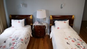 A hotel room with two single beds, a nightstand with a lamp, and a wooden dresser.
