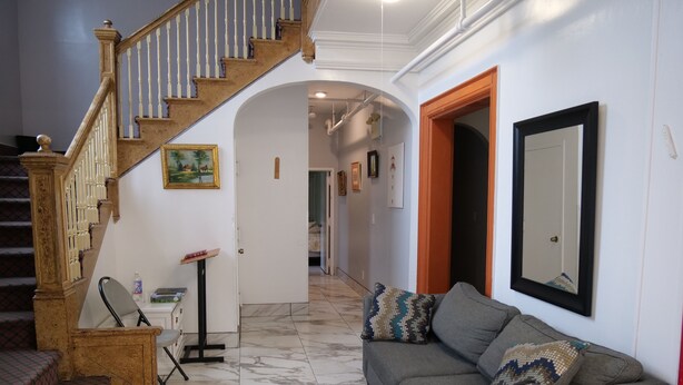 A spacious living area with a staircase, a sofa with patterned cushions, and a framed mirror on the wall.