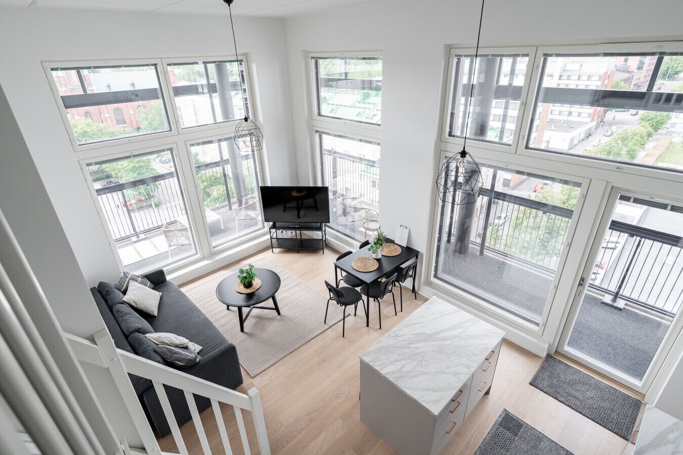 A modern living room with a sofa, dining table, TV, and large windows offering city views.