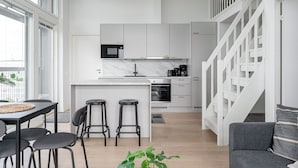 A modern kitchen with white cabinets, a marble countertop, and a black oven. There is a dining area with a table and chairs, and a staircase leading to an upper level. - 3BR Loft Penthouse w/ Balcony & Sauna (Tampere)