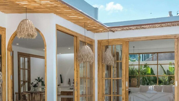 Ein moderner Poolbereich im Freien mit Sitzgelegenheit, einem Esstisch und einem durch große Fenster einsehbaren Schlafzimmer.
