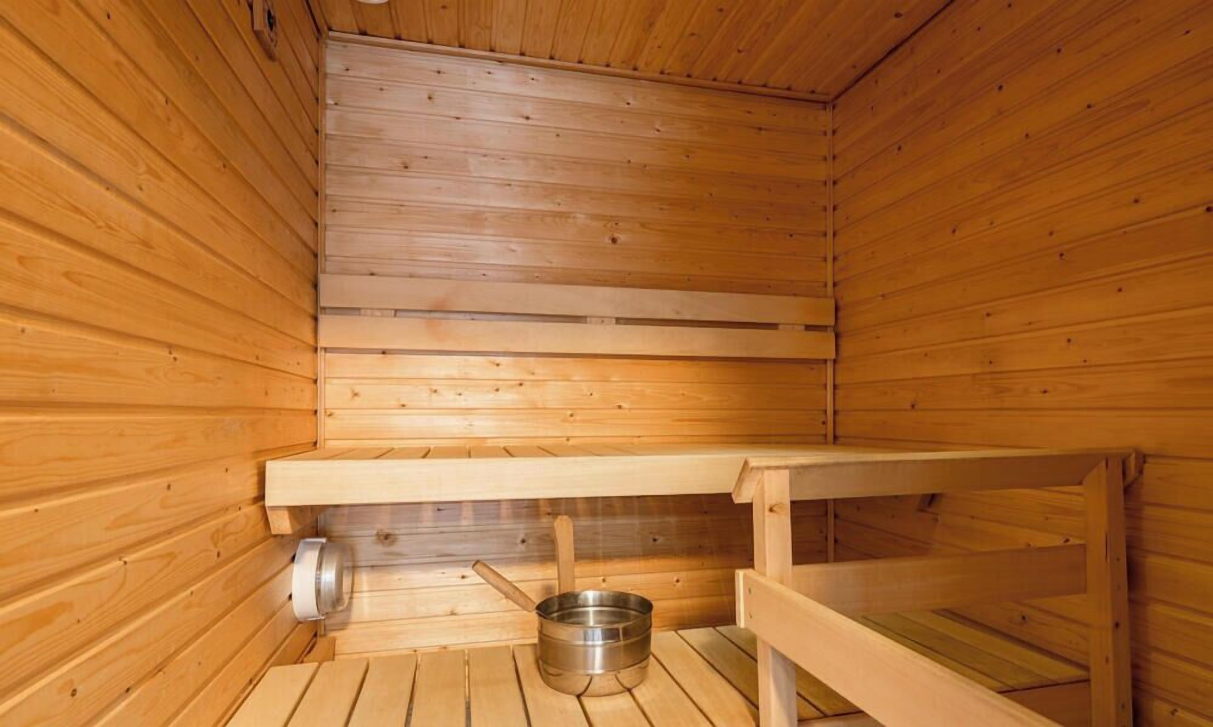 A sauna with wooden walls and benches, a metal basin, and a bench with a towel.