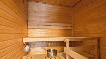 A sauna with wooden walls and benches, a metal basin, and a bench with a towel.