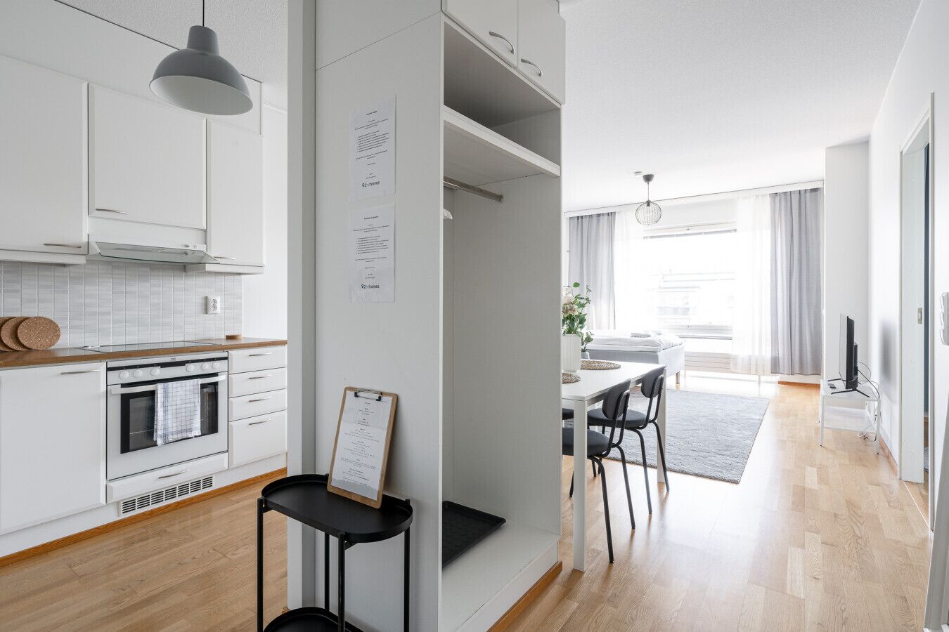 Moderni keittiö, jossa on valkoiset kaapit, sisäänrakennettu uuni sekä ruokailutila pöydän ja tuolien kera.