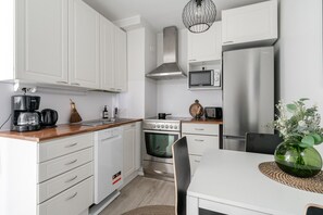 A modern kitchen with white cabinets, a stainless steel refrigerator, a microwave, a stove, and a coffee maker.