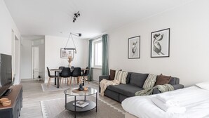 A modern living room with a sofa, a coffee table, a TV, and a dining area with chairs and a table.