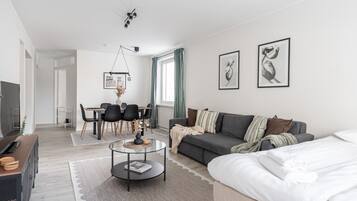 A modern living room with a sofa, a coffee table, a TV, and a dining area with chairs and a table.