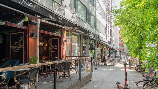 An outdoor café with wicker chairs and tables, a bike parking area, and a building with 'Freixenet' signage.