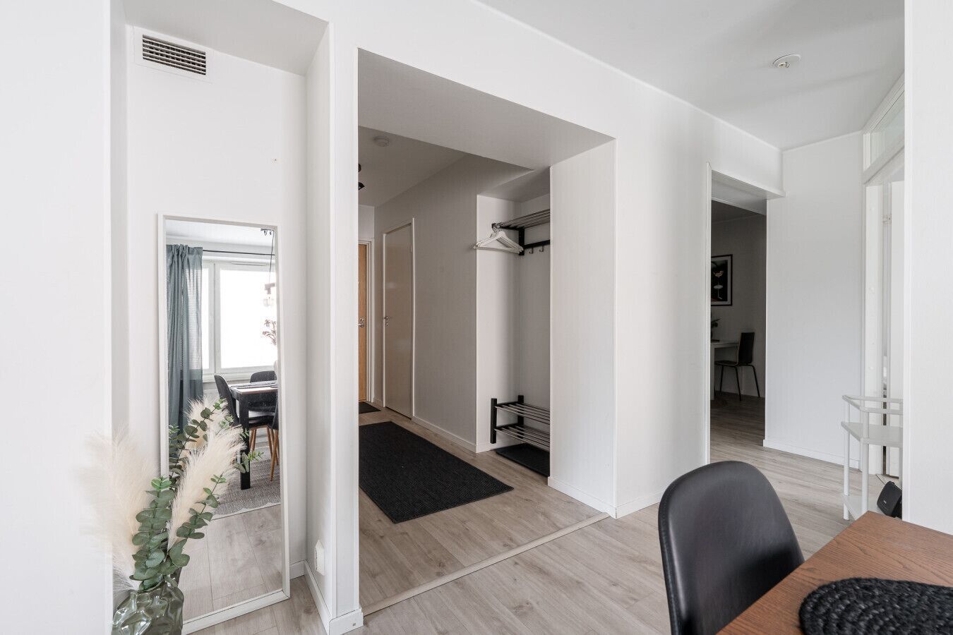A modern interior with a dining area, a hallway leading to a bedroom, and a bathroom with a towel rack.