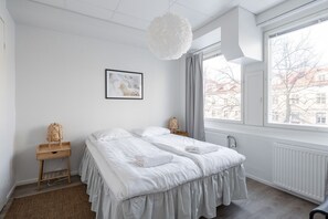 Ein modernes Schlafzimmer mit einem großen Bett, einem Nachttisch mit Lampe, einem Fenster mit Blick auf Gebäude und einer Hängelampe.