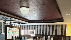 A spacious dining area with a high ceiling, patterned wall panels, and a central chandelier. - Park Square Hotel And Banquet  (Moradabad)