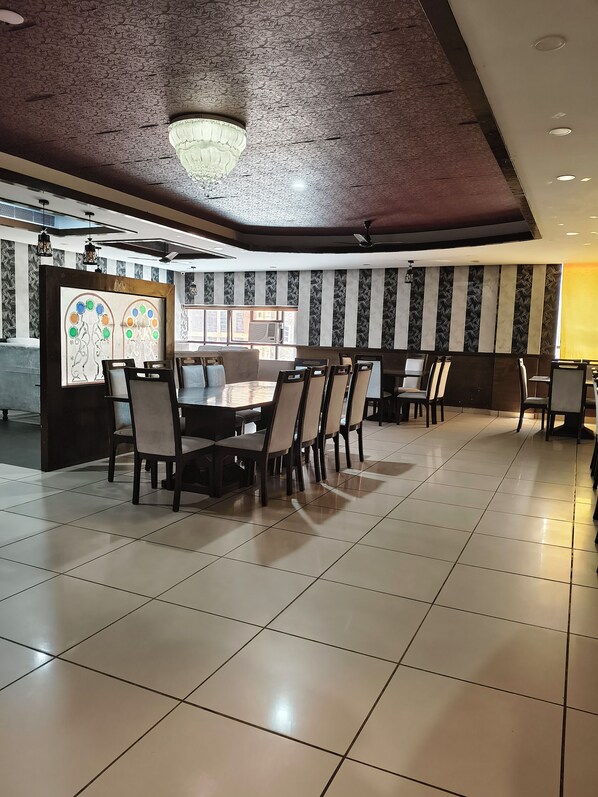 A spacious dining area with a high ceiling, patterned wall panels, and a central chandelier.