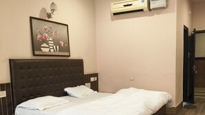 A bedroom with a large bed, a nightstand, a bedside table, an air conditioning unit, and a framed picture on the wall. - Park Square Hotel And Banquet  (Moradabad)