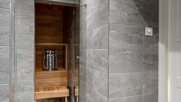 A modern bathroom with grey tiles, a wooden bench, and a glass shower enclosure. - Renovated 1BR at Main Square | Sauna & Parking (Tampere)