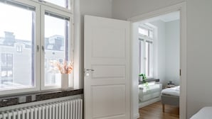 A bedroom with a large window, a radiator, a white door, and a view of the city. - Renovated 1BR at Main Square | Sauna & Parking (Tampere)