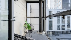 A modern balcony with a potted plant, a chair, and a glass railing.