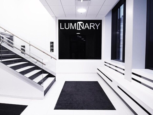 Un interior moderno con una escalera, una alfombra negra y un cartel que dice 'LUMINARY'.