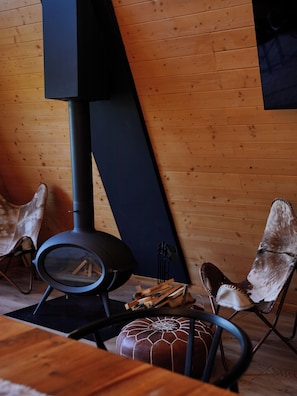 A room with a wood-burning stove, a chair, and a table. - Vino Chalets (Bran)