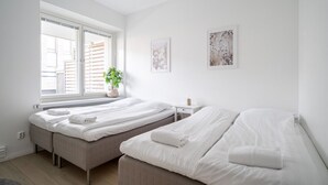 Un dormitorio moderno con dos camas, una ventana con persianas, una mesita de noche con lámpara y una planta en maceta.
